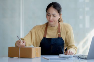 Bir e-ticaret şirketini işleten kadın, onlara göndermeden önce müşterilerin bir listesini kağıda yazıyor. Web sitelerinde ve sosyal medyada bir e-ticaret şirketi işletiyor. Çevrimiçi ürün satma kavramı.