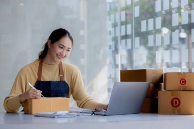 Woman who runs an e-commerce business is writing a list of customers on paper before shipping to them, she runs an e-commerce business on websites and social media. Concept of selling products online.