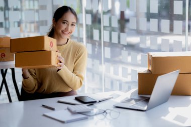 A beautiful Asian business owner opens an online store, she is checking orders from customers, sending goods through a courier company, concept of a woman opening an online business.