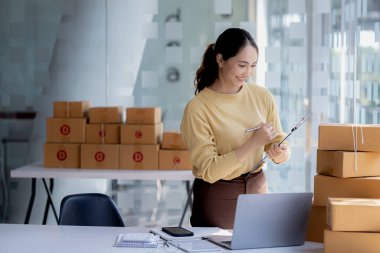 Bir çevrimiçi mağazanın sahibi, paketlenmiş ürünlerin siparişlerini web sitesinden sipariş edildiği gibi müşterilere teslimata hazırlamak için kontrol etmektedir. Çevrimiçi satış ve online alışveriş kavramları.