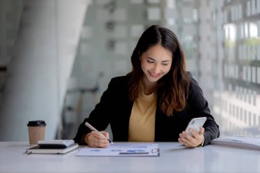 Cep telefonundan mali bilgilere bakan genç bir iş kadını, şirketin mali belgelerini kontrol ediyor, yeni kurulan bir şirketin kadın yöneticisidir. Mali yönetim kavramı.