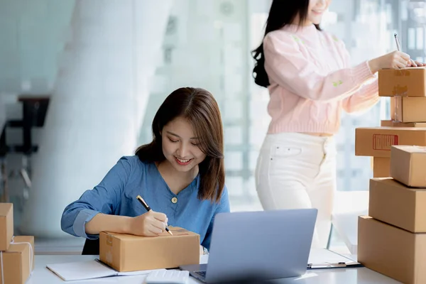 Two owners of an online store on the website are preparing parcels to send to customers following orders from the web page, they check the information and prepare for delivery to the customers.