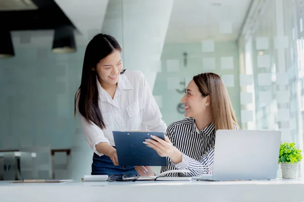 Two women looking at information on their laptops, two business women discussing brainstorming and implementation plans, form a partnership to form a startup. Management concept of startup company.