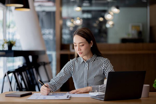 A beautiful Asian businesswoman sitting in her private office, she is checking company financial documents, she is a female executive of a startup company. Concept of financial management.