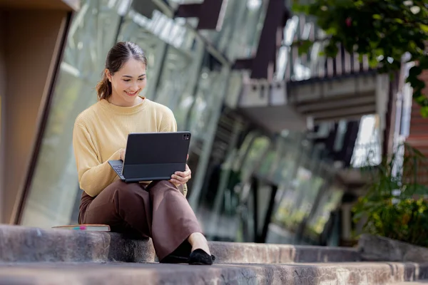 Üniversite binasının merdivenlerinde tablet kullanan Asyalı bir kadın, kız öğrenci, sınıfa giren kız öğrenci. Üniversite eğitimi kavramı.