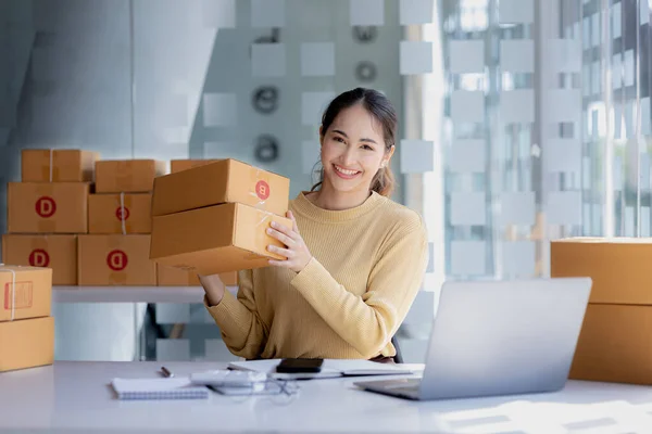 A beautiful Asian business owner opens an online store, she is checking orders from customers, sending goods through a courier company, concept of a woman opening an online business.