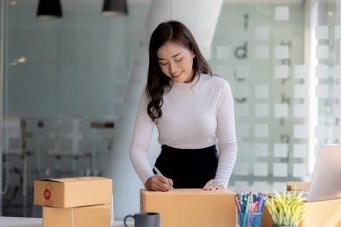 Bir e-ticaret şirketini işleten kadın, onlara göndermeden önce müşterilerin bir listesini kağıda yazıyor. Web sitelerinde ve sosyal medyada bir e-ticaret şirketi işletiyor. Çevrimiçi ürün satma kavramı.