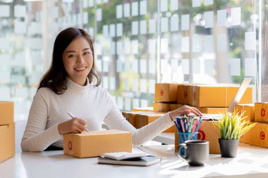 Bir e-ticaret şirketini işleten kadın, onlara göndermeden önce müşterilerin bir listesini kağıda yazıyor. Web sitelerinde ve sosyal medyada bir e-ticaret şirketi işletiyor. Çevrimiçi ürün satma kavramı.