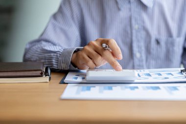 Bir şirketin mali belgelerindeki rakamları hesaplamak için hesap makinesi kullanan bir işadamı, şirketin nasıl büyüyeceğini planlamak için tarihsel finansal verileri analiz ediyor. Mali konsept.