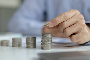 business man is stacking coins on top of the coin pile on the highest row. Placing coins in a row from low to high is comparable to saving money to grow more. Money saving ideas for investing in funds
