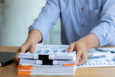 Ofis çalışanı şirkette çalışıyor, evrak işlerine başlamak için masasındaki evrakları düzenliyor, maliye bölümünde çalışıyor ve mali beyannameleri hazırlıyor..