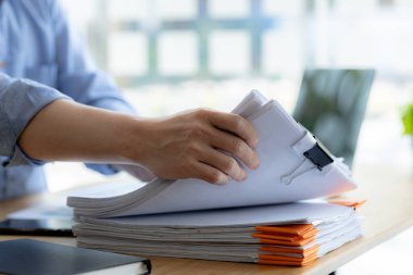 Ofis çalışanı şirkette çalışıyor, evrak işlerine başlamak için masasındaki evrakları düzenliyor, maliye bölümünde çalışıyor ve mali beyannameleri hazırlıyor..