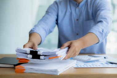 Ofis çalışanı şirkette çalışıyor, evrak işlerine başlamak için masasındaki evrakları düzenliyor, maliye bölümünde çalışıyor ve mali beyannameleri hazırlıyor..