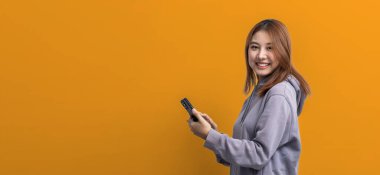 İzole edilmiş arka planda cep telefonu tutan güzel Asyalı kadının portresi, reklam ve tabela için kullanılan portre konsepti, sarı arka planda izole edilmiş, kopyalama alanı.