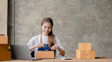 Paketi müşteri kutusuna bağlayan Asyalı bir kadın, çevrimiçi bir mağazası var, özel bir nakliye şirketi aracılığıyla paketleyip gönderiyor. Çevrimiçi satış ve online alışveriş kavramları.