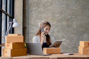 Güzel Asyalı işyeri sahibi çevrimiçi bir dükkan açıyor siparişi onaylamak için bir müşteriyle telefonda konuşuyor, malları kurye şirketi aracılığıyla gönderiyor, bir kadının internet üzerinden iş kurma kavramı....