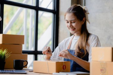 Paketi müşteri kutusuna bağlayan Asyalı bir kadın, çevrimiçi bir mağazası var, özel bir nakliye şirketi aracılığıyla paketleyip gönderiyor. Çevrimiçi satış ve online alışveriş kavramları.