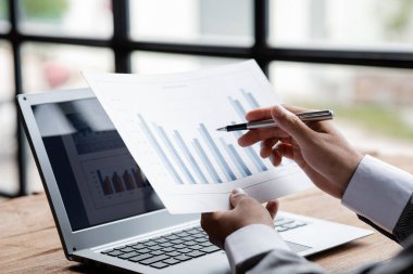 Yakın plan işadamı elinde bir kalemle bir şirketin mali belgesinin bar tablosuna işaret ederek şirketin nasıl büyüyeceğini planlamak için tarihi mali verileri analiz ediyor. Mali konsept.