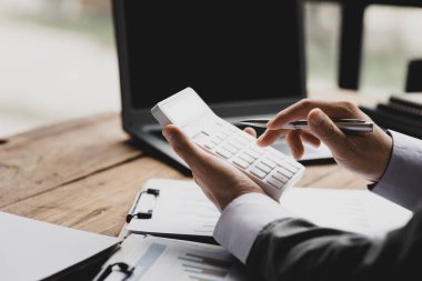 Bir şirketin mali belgelerindeki rakamları hesaplamak için hesap makinesi kullanan bir işadamı, şirketin nasıl büyüyeceğini planlamak için tarihsel finansal verileri analiz ediyor. Mali konsept.