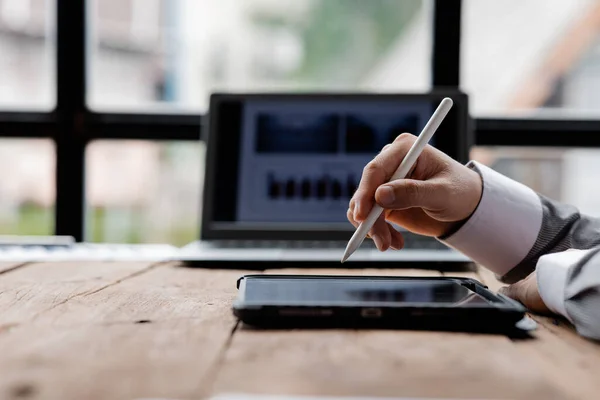 Person holding pen pointing at tablet placed on desk, business man looking at information on tablet and using tablet to communicate with company team through messaging and email programs.