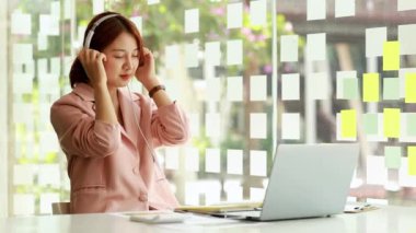 Güzel bir Asyalı kadın, stresi azaltmak için işten molada müzik dinliyor, yeni başlayan şirketin pazarlama müdürü, kadın lider, yönetici, CEO 'su. Kadın Liderlik Konsepti.