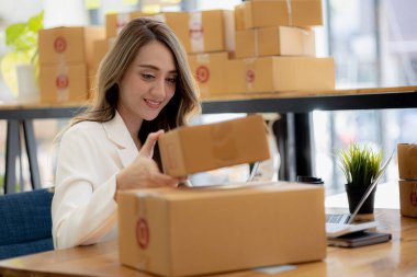 Bir çevrimiçi mağazanın sahibi, paketlenmiş ürünlerin siparişlerini web sitesinden sipariş edildiği gibi müşterilere teslimata hazırlamak için kontrol etmektedir. Çevrimiçi satış ve online alışveriş kavramları.