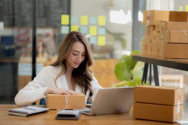 Bir e-ticaret şirketini işleten kadın, onlara göndermeden önce müşterilerin bir listesini kağıda yazıyor. Web sitelerinde ve sosyal medyada bir e-ticaret şirketi işletiyor. Çevrimiçi ürün satma kavramı.