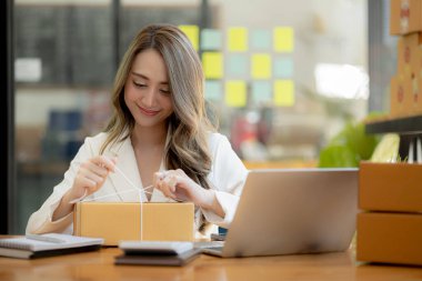 Paketi müşteri kutusuna bağlayan Asyalı bir kadın, çevrimiçi bir mağazası var, özel bir nakliye şirketi aracılığıyla paketleyip gönderiyor. Çevrimiçi satış ve online alışveriş kavramları.