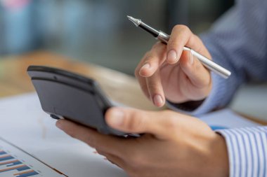 Beyaz hesap makinesi kullanan bir iş adamının yakın plan çekimi, bir şirketin mali dökümanındaki sayısal verileri inceleyen bir finans işadamı, sayıların doğruluğunu doğrulamak için bir hesap makinesi kullanır..