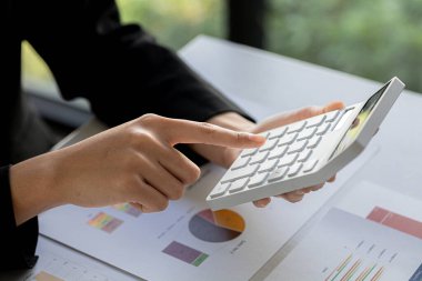 Bir şirketin mali belgelerindeki rakamları hesaplamak için hesap makinesi kullanan bir işadamı, şirketin nasıl büyüyeceğini planlamak için tarihsel finansal verileri analiz ediyor. Mali konsept.