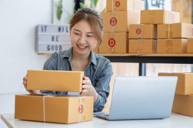 Bir çevrimiçi mağazanın sahibi, paketlenmiş ürünlerin siparişlerini web sitesinden sipariş edildiği gibi müşterilere teslimata hazırlamak için kontrol etmektedir. Çevrimiçi satış ve online alışveriş kavramları.