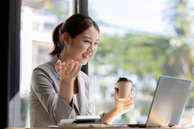 Beautiful Asian businesswoman sitting in her private office, she is talking to her partner via video call on her laptop, she is a female executive of a startup company. Concept of financial management