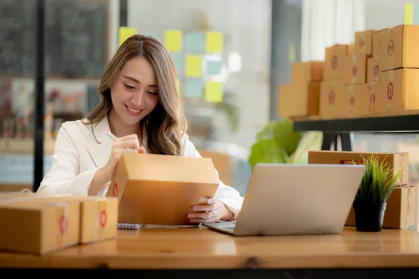 Woman who runs an e-commerce business is writing a list of customers on paper before shipping to them, she runs an e-commerce business on websites and social media. Concept of selling products online.