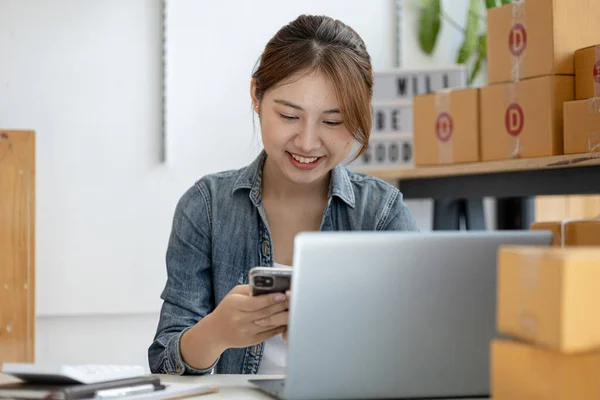 A beautiful Asian business owner opens an online store, she is checking orders from customers, sending goods through a courier company, concept of a woman opening an online business.