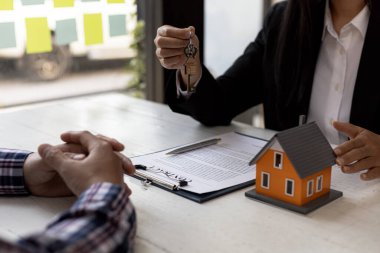 Bir ev kiralama şirketi çalışanı kira sözleşmesi imzalamayı kabul eden bir müşteriye kira sözleşmesinin detaylarını ve şartlarını açıklayan ev anahtarlarını teslim ediyor. Ev ve gayrimenkul kiralama fikirleri.