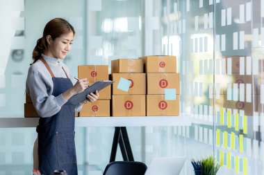 Bir çevrimiçi mağazanın sahibi, paketlenmiş ürünlerin siparişlerini web sitesinden sipariş edildiği gibi müşterilere teslimata hazırlamak için kontrol etmektedir. Çevrimiçi satış ve online alışveriş kavramları.