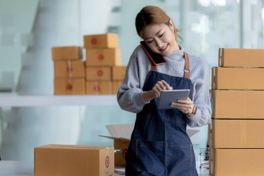 Asyalı bir kadın siparişi doğrulamak için bir müşteriyle telefonda konuşuyor, bir online mağazası var, özel bir nakliye şirketi aracılığıyla paketleyip gönderiyor. Çevrimiçi satış ve online alışveriş kavramları.