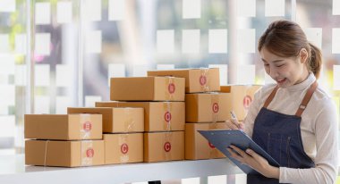 Bir çevrimiçi mağazanın sahibi, paketlenmiş ürünlerin siparişlerini web sitesinden sipariş edildiği gibi müşterilere teslimata hazırlamak için kontrol etmektedir. Çevrimiçi satış ve online alışveriş kavramları.