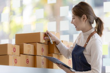 Bir çevrimiçi mağazanın sahibi, paketlenmiş ürünlerin siparişlerini web sitesinden sipariş edildiği gibi müşterilere teslimata hazırlamak için kontrol etmektedir. Çevrimiçi satış ve online alışveriş kavramları.