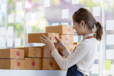 Bir çevrimiçi mağazanın sahibi, paketlenmiş ürünlerin siparişlerini web sitesinden sipariş edildiği gibi müşterilere teslimata hazırlamak için kontrol etmektedir. Çevrimiçi satış ve online alışveriş kavramları.