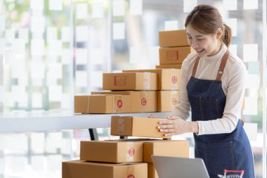 Bir çevrimiçi mağazanın sahibi, paketlenmiş ürünlerin siparişlerini web sitesinden sipariş edildiği gibi müşterilere teslimata hazırlamak için kontrol etmektedir. Çevrimiçi satış ve online alışveriş kavramları.