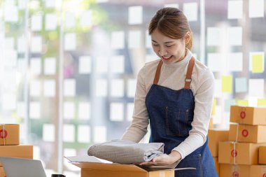 Bir çevrimiçi mağazanın sahibi müşterilere internet sitesinden verilen siparişlere göre teslimata hazırlanmak için ürünleri paket kutularına koyuyor. Çevrimiçi satış ve online alışveriş kavramları.
