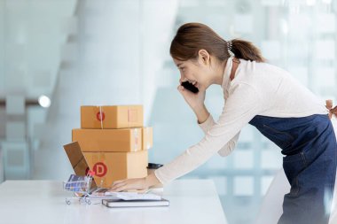 Asyalı bir kadın siparişi doğrulamak için bir müşteriyle telefonda konuşuyor, bir online mağazası var, özel bir nakliye şirketi aracılığıyla paketleyip gönderiyor. Çevrimiçi satış ve online alışveriş kavramları.
