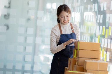 Bir çevrimiçi mağazanın sahibi, paketlenmiş ürünlerin siparişlerini web sitesinden sipariş edildiği gibi müşterilere teslimata hazırlamak için kontrol etmektedir. Çevrimiçi satış ve online alışveriş kavramları.