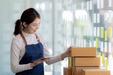 Bir çevrimiçi mağazanın sahibi, paketlenmiş ürünlerin siparişlerini web sitesinden sipariş edildiği gibi müşterilere teslimata hazırlamak için kontrol etmektedir. Çevrimiçi satış ve online alışveriş kavramları.