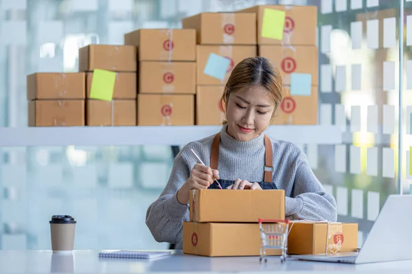 Woman who runs an e-commerce business is writing a list of customers on paper before shipping to them, she runs an e-commerce business on websites and social media. Concept of selling products online.