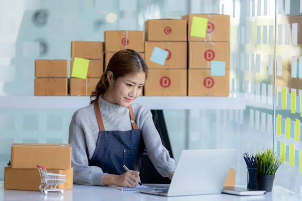 A beautiful Asian business owner opens an online store, she is checking orders from customers, sending goods through a courier company, concept of a woman opening an online business.