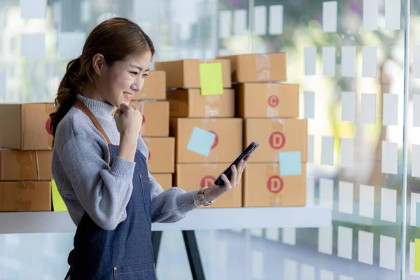 A beautiful Asian business owner opens an online store, she is checking orders from customers, sending goods through a courier company, concept of a woman opening an online business.