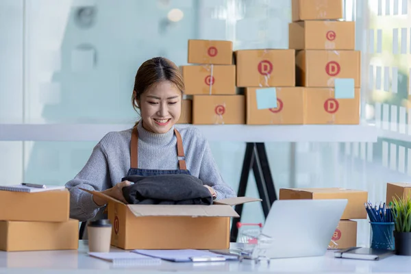 The owner of an online store is packing products into parcel boxes to prepare for delivery to customers according to orders through the website. Online selling and online shopping concepts.