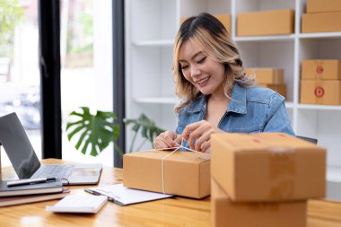 Paketi müşteri kutusuna bağlayan Asyalı bir kadın, çevrimiçi bir mağazası var, özel bir nakliye şirketi aracılığıyla paketleyip gönderiyor. Çevrimiçi satış ve online alışveriş kavramları.